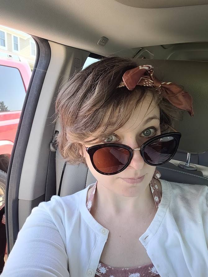 Image of a women with short brown hair and large sunglasses sitting in a car.